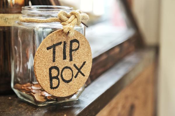 Glass jar with some coins in and a label reading Tip Box