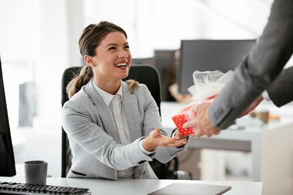 Woman sat at desk being passed a Christmas present