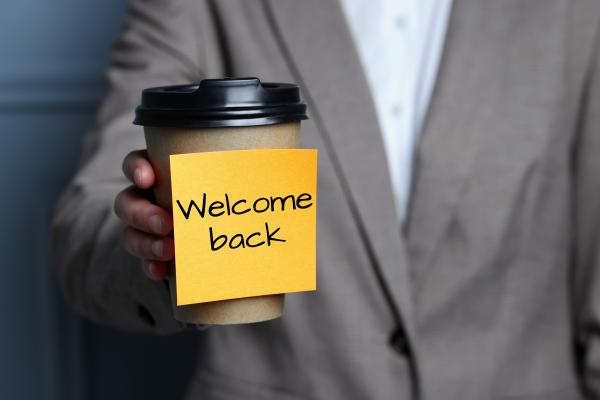 Person holding coffee cup with a sticky note on reading "welcome back'