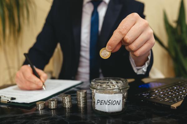 Man in suit doing paperwork at a desk and adding individual coins into a jar from piles  of coins infront of him