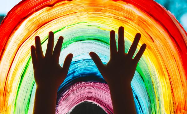 Child's hands raised silhoutted against a painted rainbow