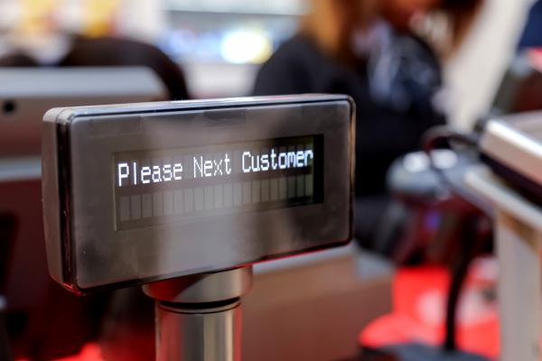 A black till sign reading 'Please next customer'.