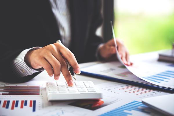 Smartly dressed woman using calculator on desk covered with documents