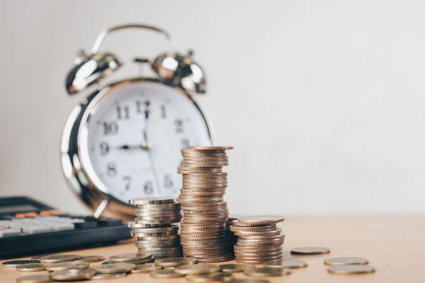 Piles of coins with traditional alarm clock in the background