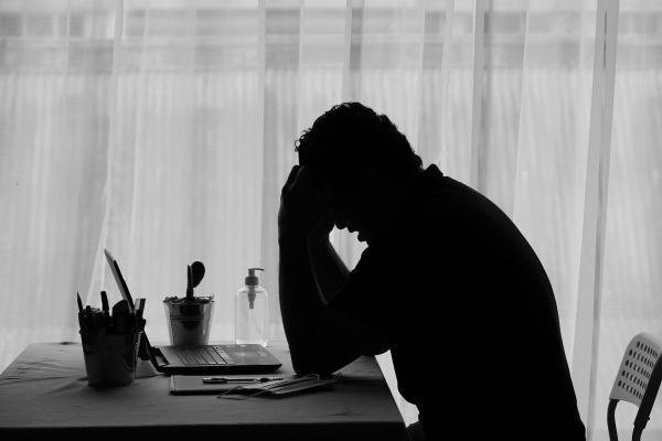 Black and white image of a man sat at a desk holding his head in his hands