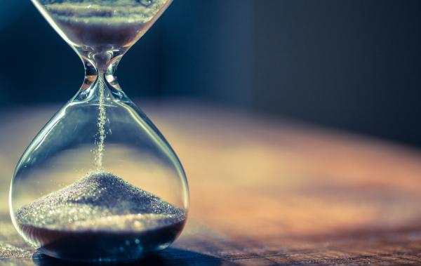 Hourglass with sand running through it, sat on a table 