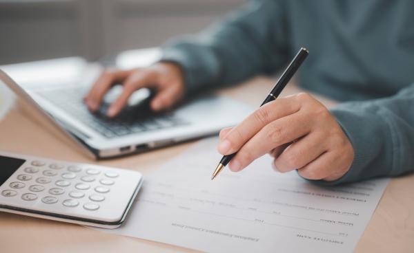 Person sat at desk with laptop and calculator completing a form 