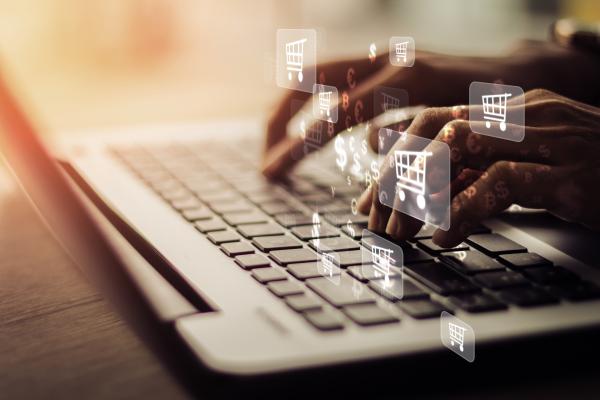 Laptop with person's hands shown typing and overlaid shopping cart symbols.