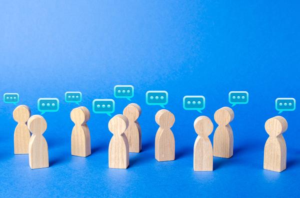 A group of wooden toys symbolising people are standing around on a blue background with little speech bubbles above to show a group in conversation