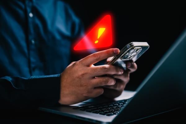 Man using mobile phone and laptop with a superimposed red exclamation mark warning symbol 