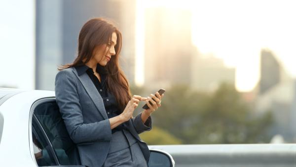 Woman leaning on car and using mobile phone