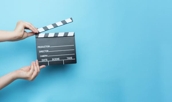 Hand holding movie clapperboard against blue background