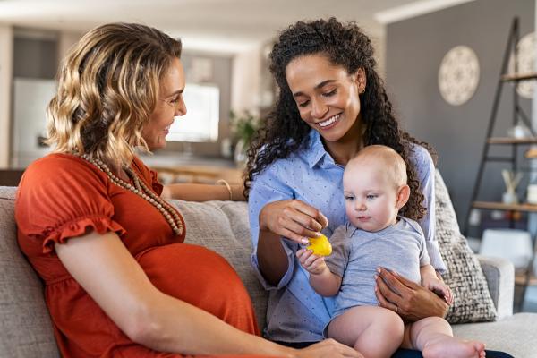 Two women sat on sofa - one pregnant, one holding a baby