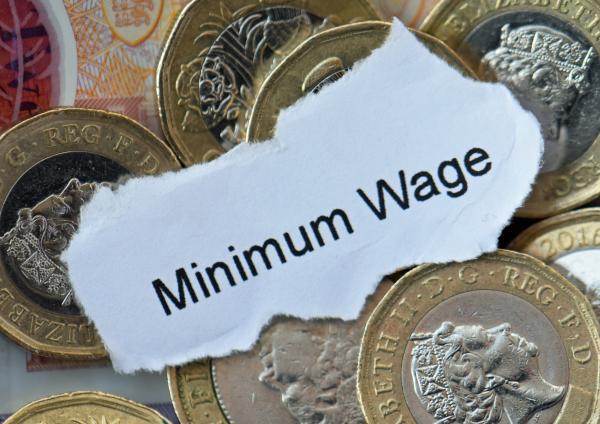 Torn piece of paper showing words "minimum wage" placed among coins