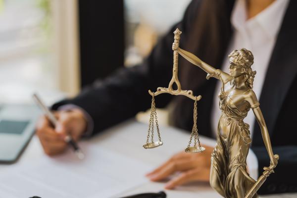 Statue of Lady Justice in foreground, with smartly dressed woman working at a desk behind