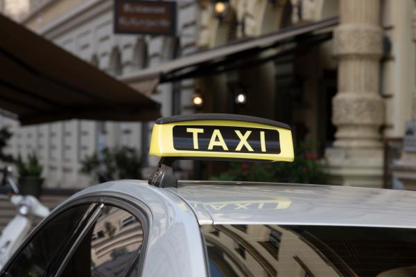 White car with yellow taxi sign on roof in city.