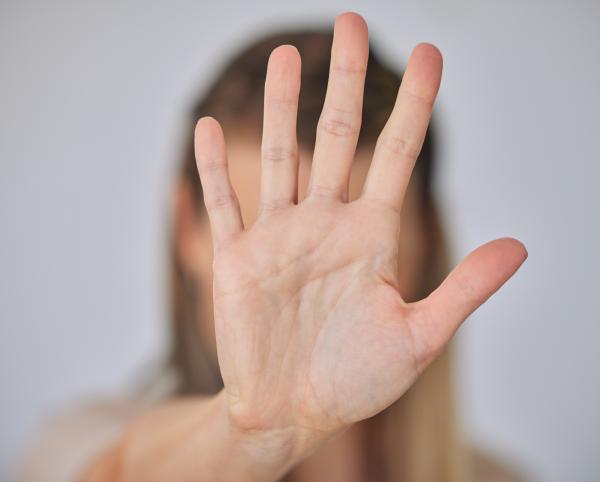 Woman raising hand in an open palmed STOP gesture, which obscures her face 