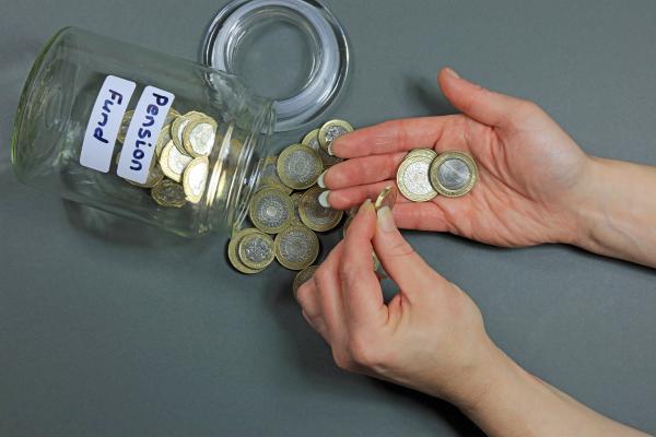 A jar of coins labelled 'pension fund' lies on its side, with hands counting out some of the coins