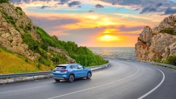 Car driving along a twisting, scenic road against a sunset 