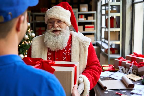 Santa Clause handing a wrapped parcel to a delivery driver