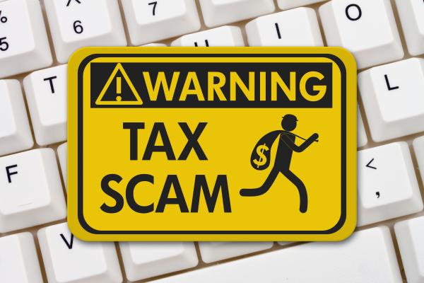 Yellow warning sign reading "Warning Tax Scam" resting on a computer keyboard