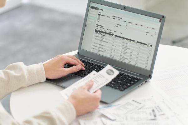 Person using a laptop and holding paper receipts