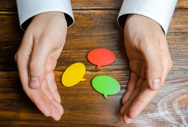 Red, yellow and green speech bubble shapes on a desk, cupped by two hands