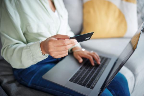 Woman using a laptop with one hand and holding a bank card with the other