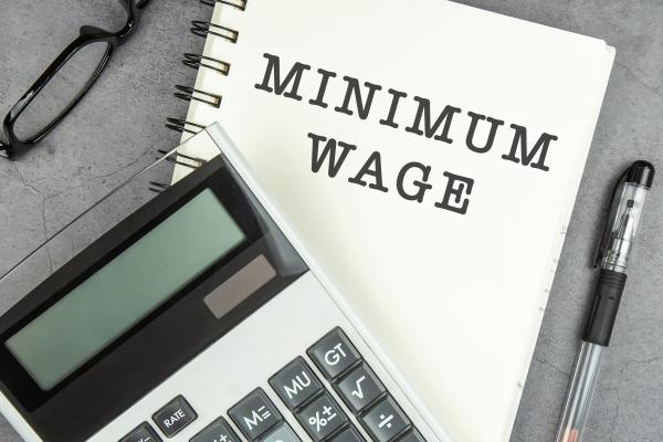 Notebook with the words "Minimum Wage" showing, with a calculator and pen next to it