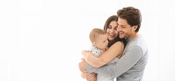 Man and woman stood facing the same way and embracing, with woman holding baby